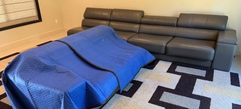 two couches in living room, one is covered with moving blankets 