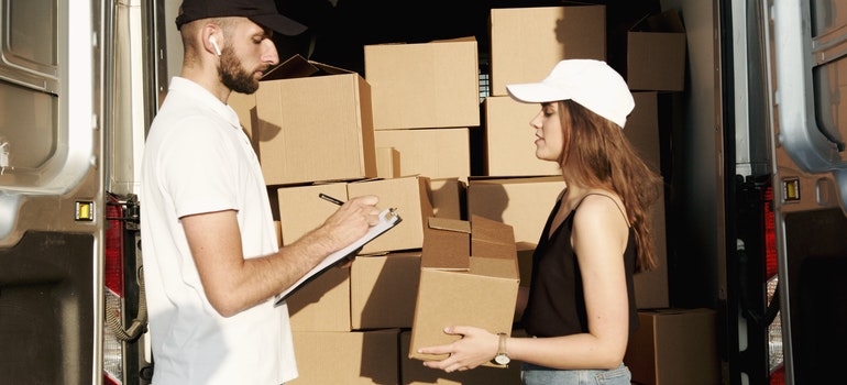 A mover and a woman next to a moving truck and packed boxes