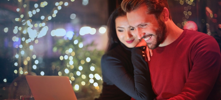A smiling couple makes a list on the computer about dating in LA vs SF.