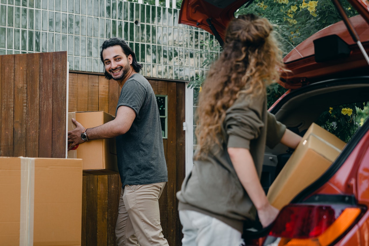 Happy couple unloading automobile with moving boxes
