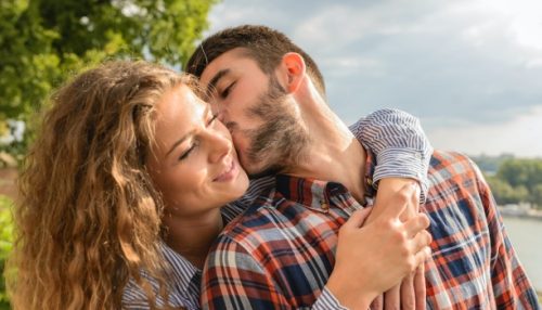 A woman hugs a man who kisses her on the cheek