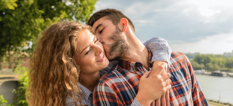 A woman hugs a man who kisses her on the cheek